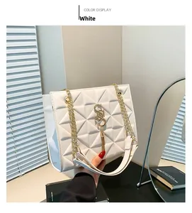Detailed view of white quilted shoulder bag with gold chain strap and metal tassel charm