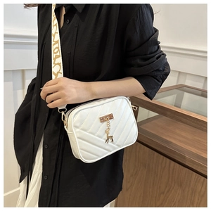 Close-up of white V-quilted crossbody bag featuring a golden deer charm and wide fabric strap
