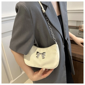Detail of cream white underarm bag with silver bow ornament and chain strap on shoulder