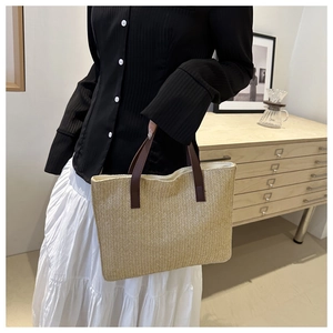 Close-up of beige woven tote bag featuring brown leather handles in a home setting