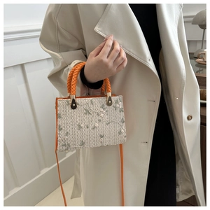 Detail of woven handbag featuring white floral embroidery and orange circular handles