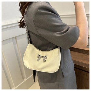 Close-up of cream underarm bag with silver bow accent on model in grey suit