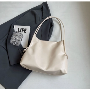 Dettaglio della borsa tote crema minimalista con nodo laterale su blazer grigio