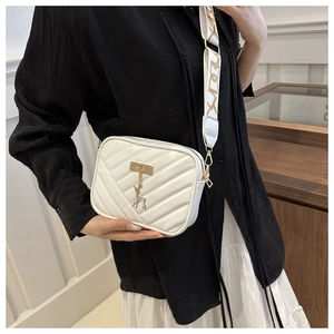 Detail view of a white quilted crossbody bag with golden deer pendant and wide strap