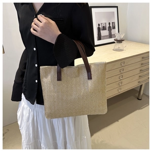 Detail of hand-woven tote bag with brown leather handles in a warm interior setting