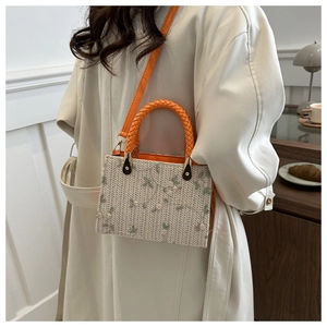 Detail of straw woven crossbody bag featuring green floral embroidery and orange handle