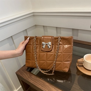 Quilted brown leather tote bag with silver bow buckle and golden chain on a table