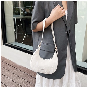 Detail of white crescent bag with stone texture, silver lettering and gold hardware