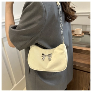 Detail of a chic cream underarm bag with a silver metal bow and shiny leather texture