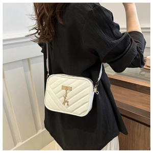 Detail of white quilted crossbody bag with golden deer pendant and wide shoulder strap