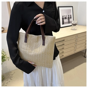 Detail of woven tote bag with beige herringbone texture and brown leather handles