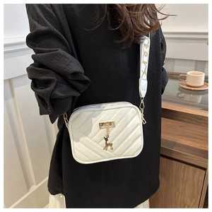 Detail of white quilted crossbody bag featuring gold deer charm and embroidered strap