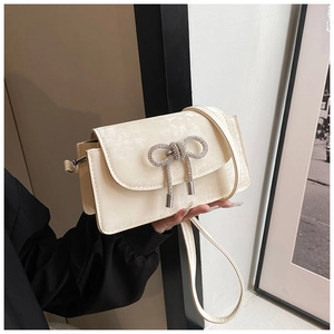 Detail of cream white crossbody bag featuring a sparkling rhinestone bow buckle