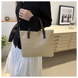 Detail view of woven straw tote bag with brown handles in a lifestyle home setting