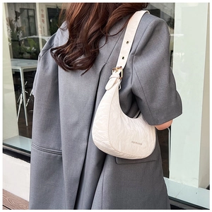 Detailed view of white crescent bag with ruched texture on a model wearing grey blazer