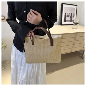 Close-up of woven straw tote bag with brown leather handles and magnetic snap closure
