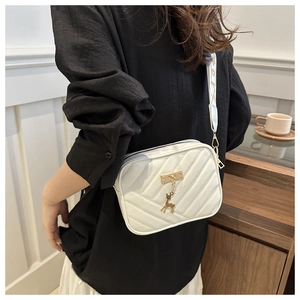 Detail of white quilted crossbody bag with golden deer charm and wide jacquard strap