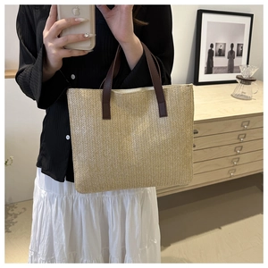 Close-up of woven straw tote bag with brown leather handles and herringbone texture
