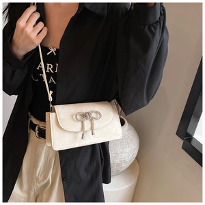 Detail of a creamy white square bag featuring a sparkling silver rhinestone bow and tassel