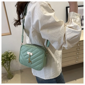 Detail of mint green quilted leather bag with golden deer pendant and wide strap