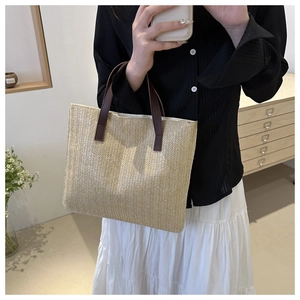 Detail of woven straw tote bag with brown leather handles held by a model indoors