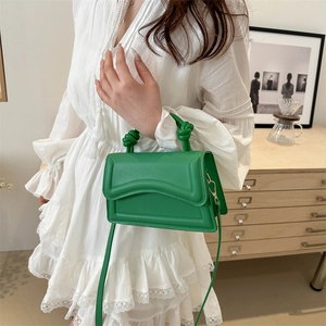 Bright green crossbody bag with knot handle and adjustable strap worn with white dress