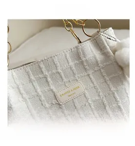 Detail of white textured tweed tote bag featuring golden chain and plush ball charm