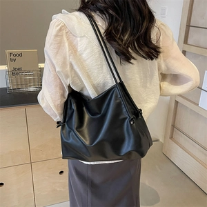 Minimalist black faux leather tote bag with drawstring knots shown on a shoulder