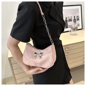 Close-up of pink velvet underarm bag featuring a silver metal bow detail and chain strap