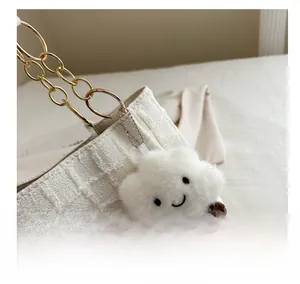 Detail of a plush cloud charm with smiley face on a white woven tote bag with gold chain