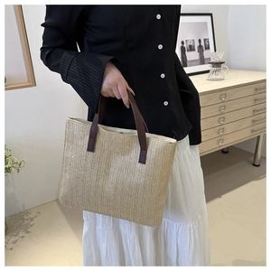 Detail of hand-woven beige tote bag featuring contrasting dark brown leather handles