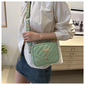 Close-up of mint green quilted camera bag with golden deer charm and wide patterned strap