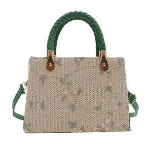 Straw tote bag with green floral embroidery and adjustable shoulder strap on white backdrop