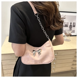 Detail of pink satin shoulder bag featuring a metallic silver bow and chain strap