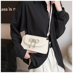 Chic cream bow shoulder bag on a model wearing a black shirt and white trousers