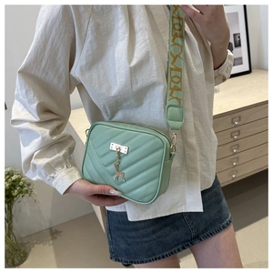 Detailed shot of mint green quilted crossbody bag with golden deer charm and wide strap