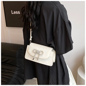 Chic white crossbody bag with sparkling rhinestone bow detail shown on a model