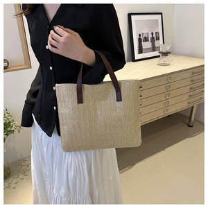 Detail of woven straw tote bag with brown leather handles in a minimalist home setting