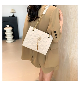 Detail of white quilted crossbody bag with gold chain strap and tassel on brown blazer