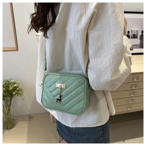 Detailed side view of mint green crossbody bag with V-quilted texture and deer charm