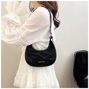 Detail of glossy black crescent shoulder bag with adjustable strap and gold hardware