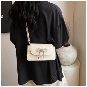 Chic cream-colored crossbody bag featuring a sparkling rhinestone bow on a minimalist flap