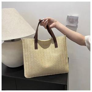 Detail of woven straw tote bag with brown leather handles and herringbone pattern