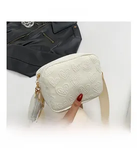 Detail of cream white crossbody bag featuring 3D heart embossing and wide fabric strap