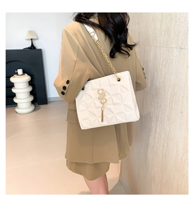 Close-up of white quilted chain bag with gold tassel logo and leather strap detail