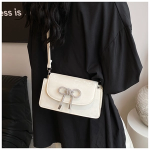 Close-up of white crossbody bag with silver rhinestone bow and metal tassels