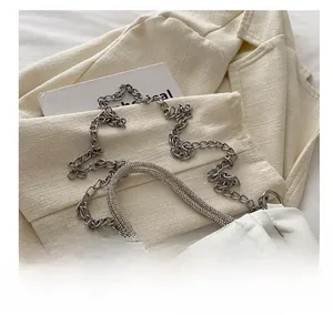Detail van witte geplooide tas met strass handvat en zilveren metalen kettingriem
