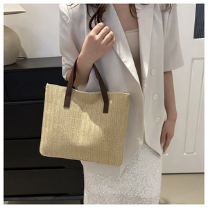 Detail view of woven straw tote bag with beige herringbone pattern and brown leather handle