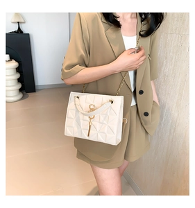 Detail of cream crossbody bag featuring geometric texture and gold tassel charm accent