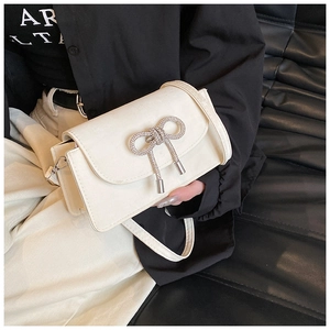 Detailed view of cream bow square bag with rhinestones on shoulder model